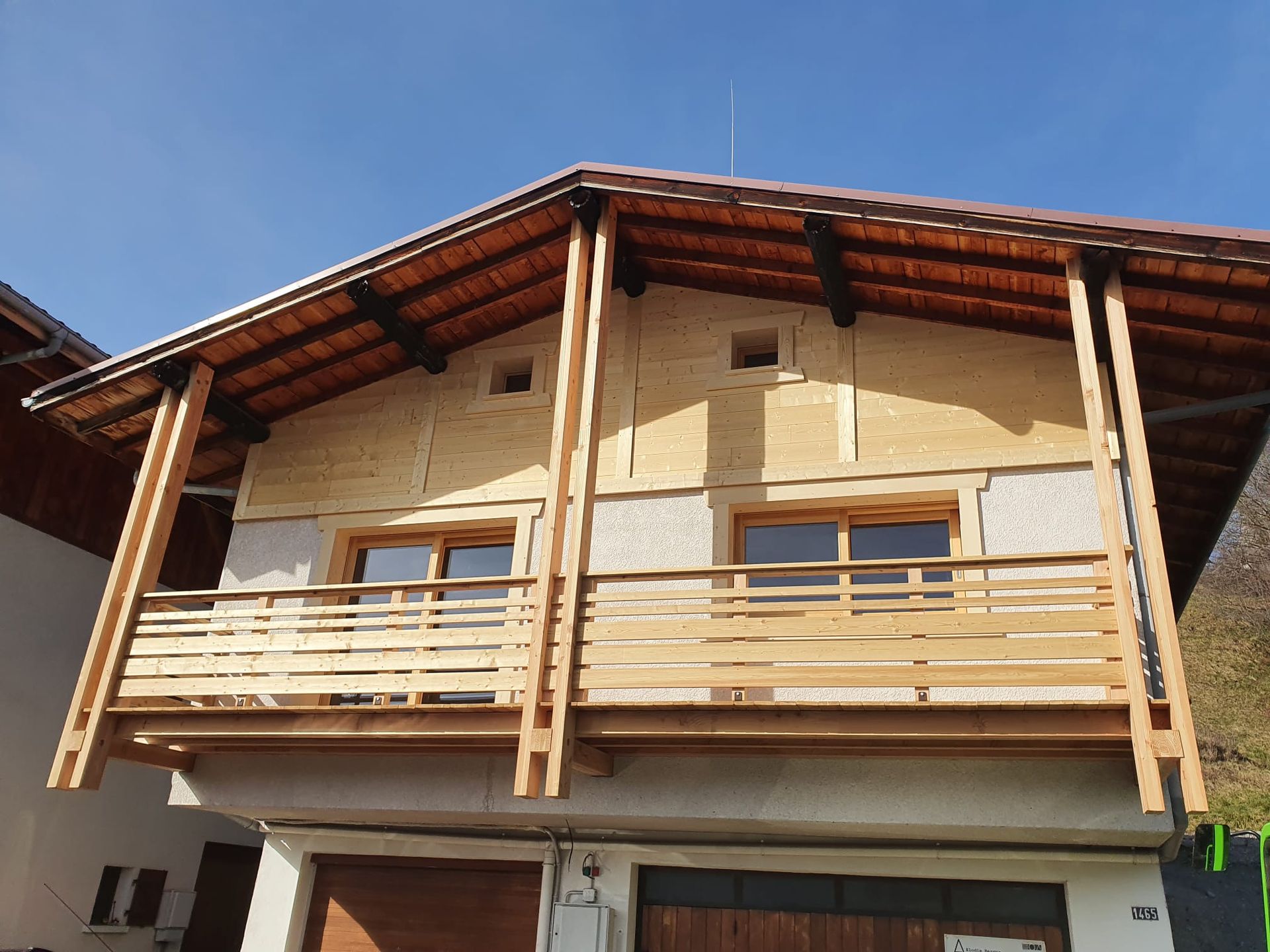 Maison à deux étages avec balcon en bois et toit en pente sous un ciel bleu