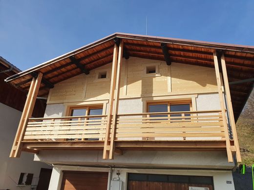 Maison à deux étages avec balcon en bois et toit en pente sous un ciel bleu