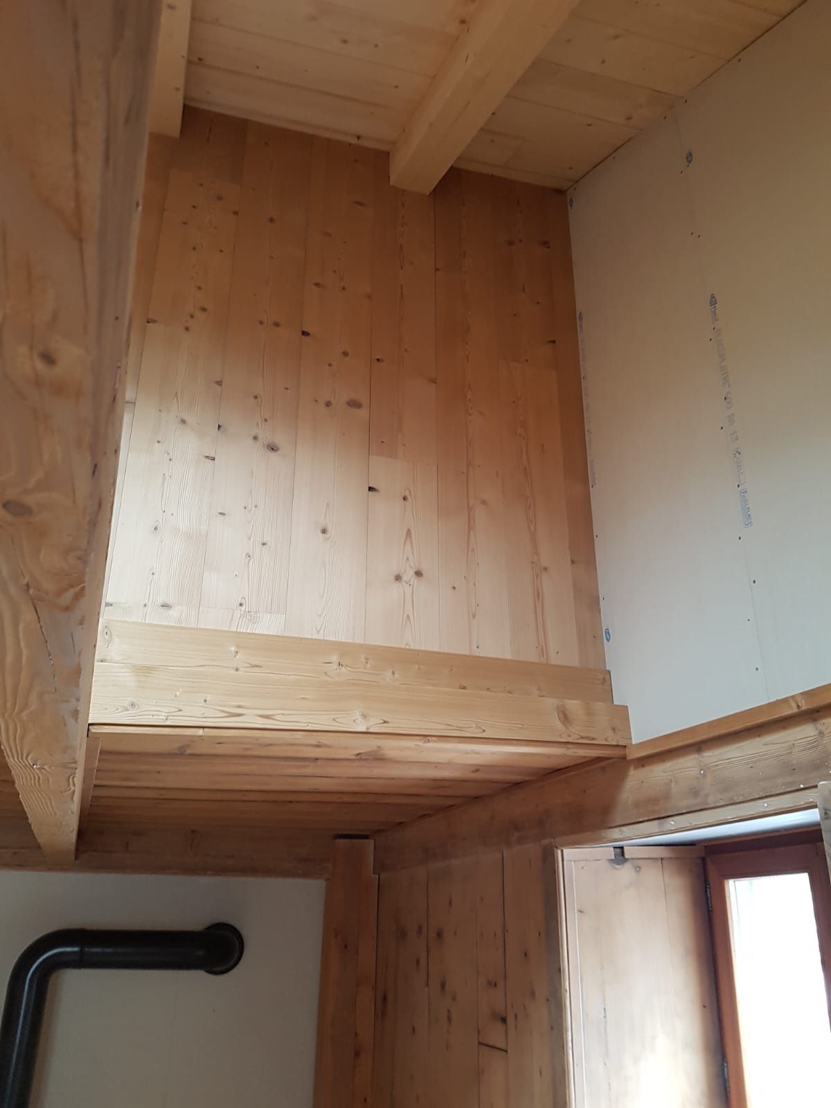 Mezzanine ou coin de rangement lambrissé au-dessus d'une porte avec une petite fenêtre en dessous.