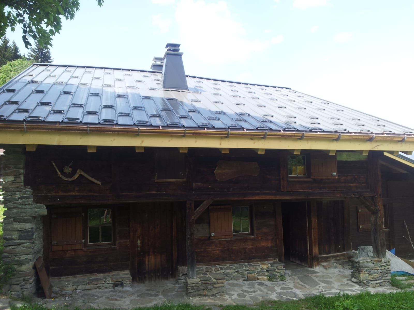 Cabane rustique en bois avec porche en pierre et toit en métal sous un ciel lumineux