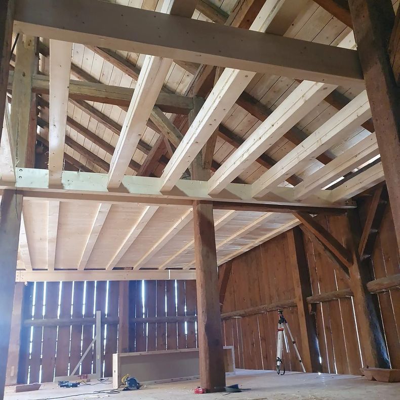 Intérieur d'une grange rustique en bois avec poutres apparentes et murs à claire-voie, vue depuis le dessous du grenier.