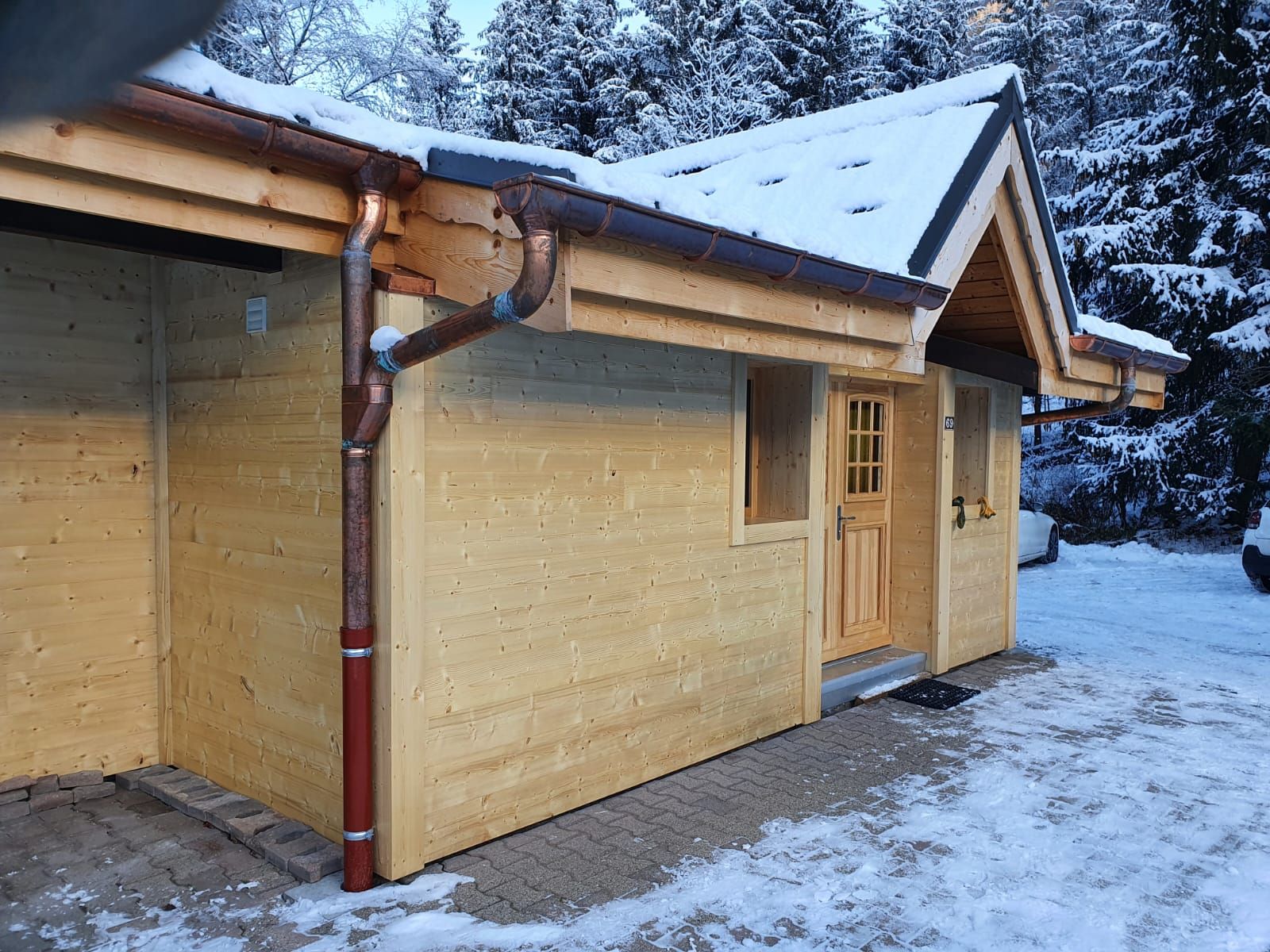 Chalet en bois enneigé, avec une porte et une gouttière brunes, à côté d'une allée en hiver