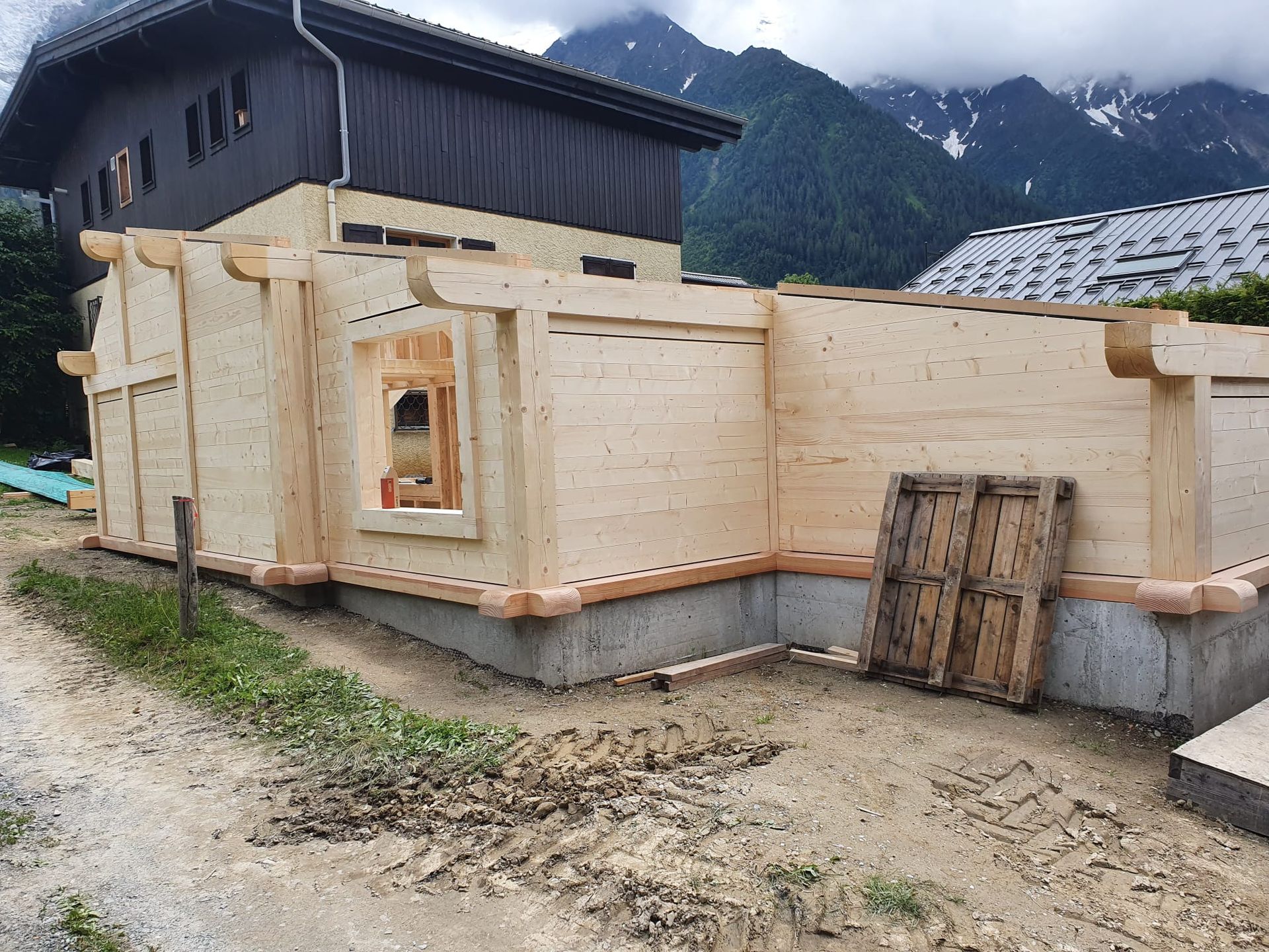 Maison en bois en construction sur des fondations en béton dans un village de montagne.