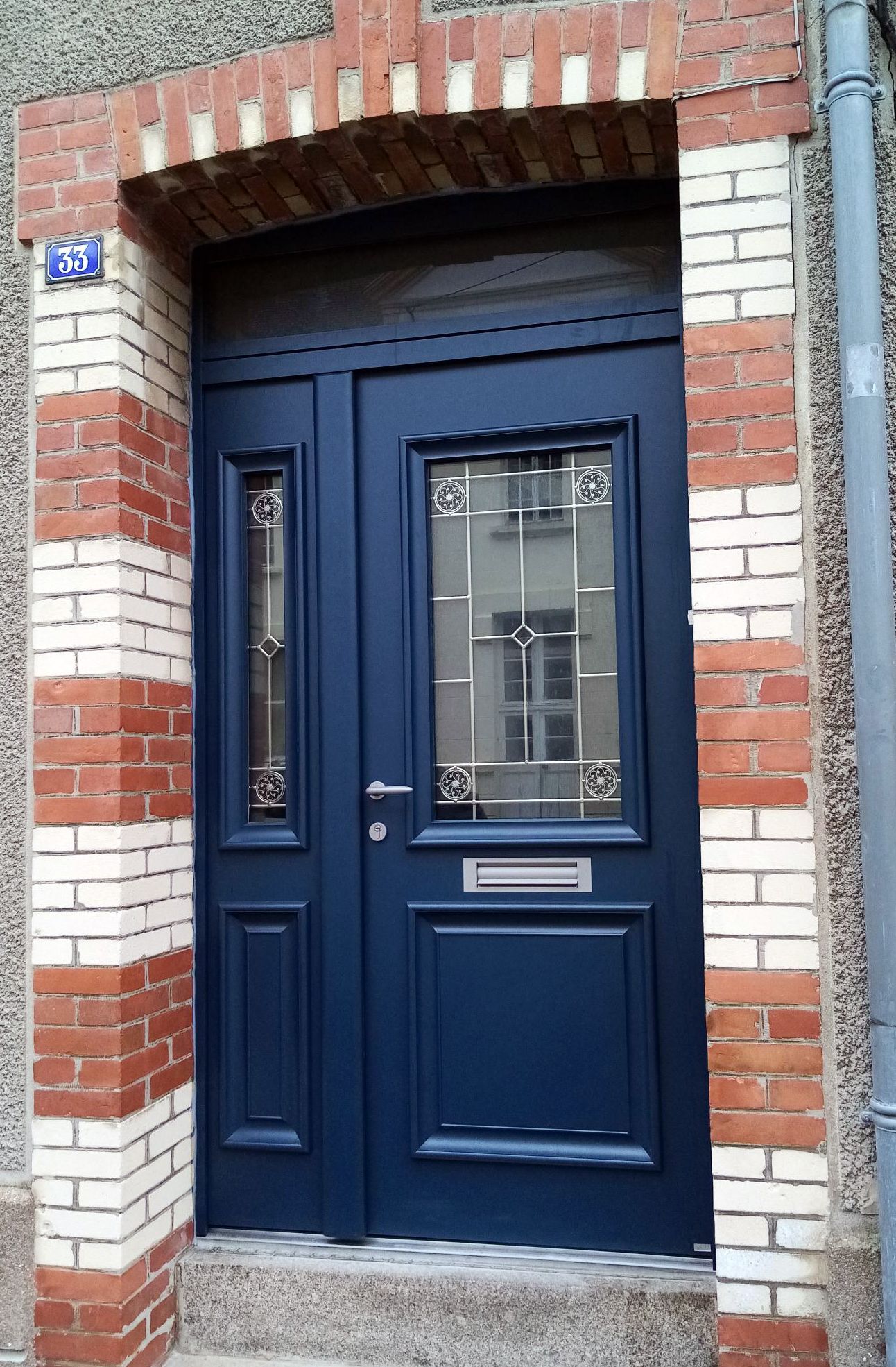 Porte d'entrée bleue avec panneaux de verre encastrée dans une entrée en briques