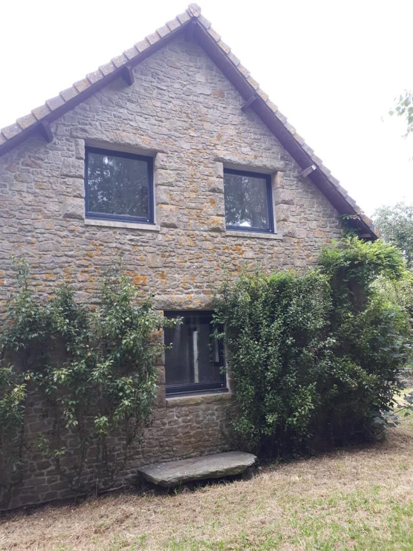 Maisonnette en pierre avec deux fenêtres à l'étage, une fenêtre au rez-de-chaussée et des arbustes recouverts de lierre devant.