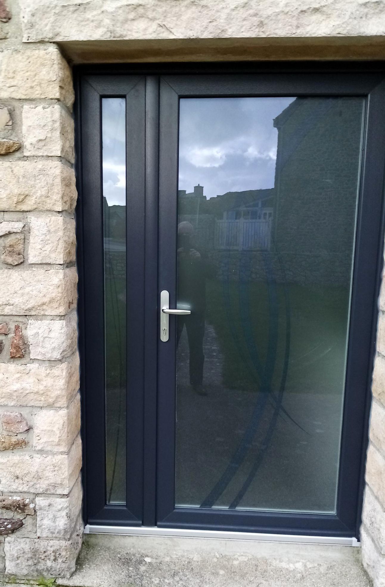 Porte d'entrée noire avec verre dépoli encastrée dans un mur de pierre, vue de l'extérieur.