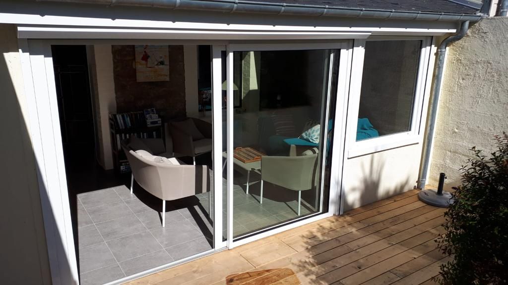 Patio couvert avec portes coulissantes en verre, une chaise blanche et une petite table à côté d'une terrasse en bois.