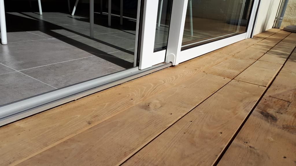 Terrasse en bois jouxtant une porte coulissante en verre par une journée ensoleillée