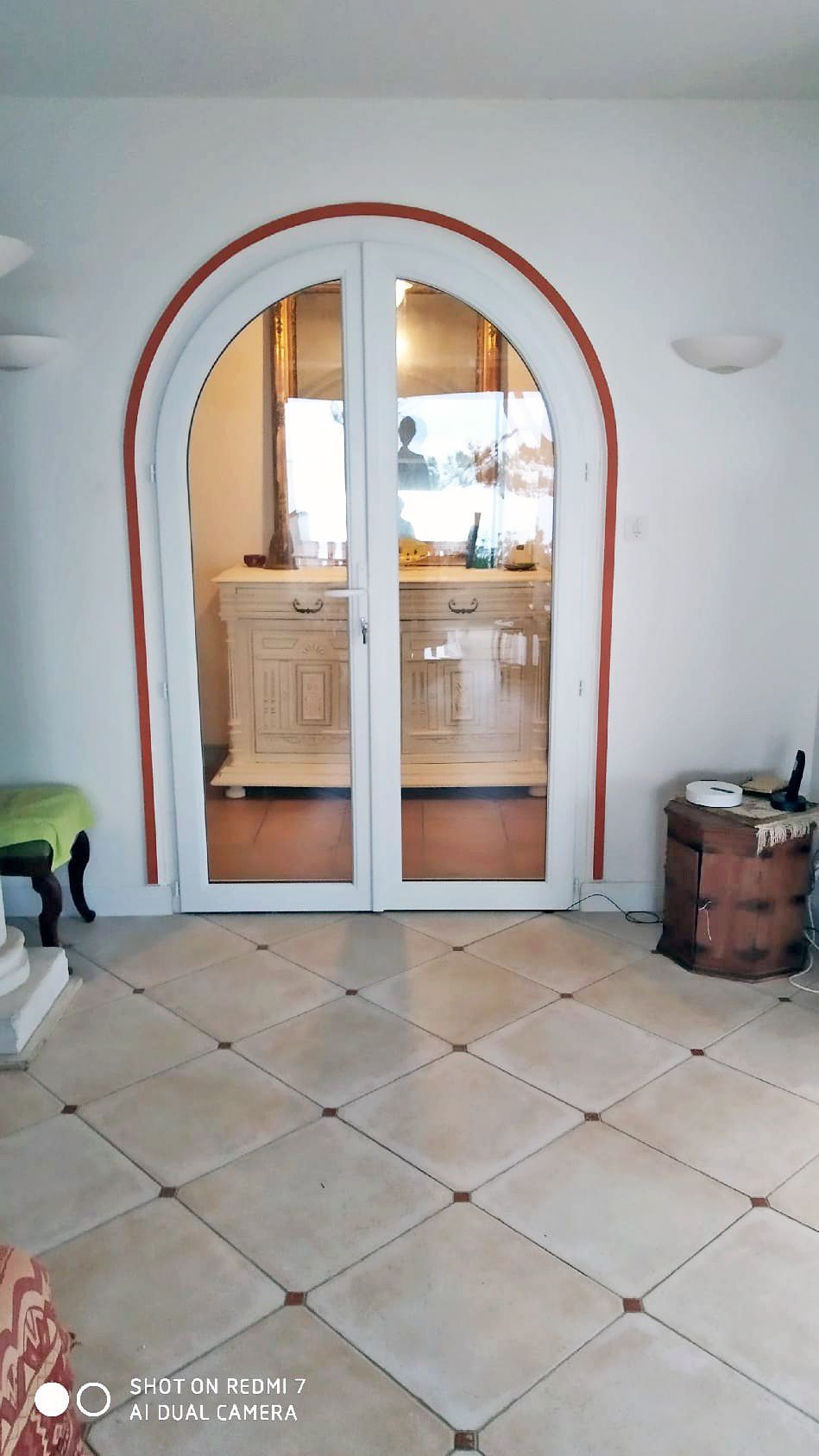 Des portes doubles blanches cintrées s'ouvrent sur une cuisine, avec un sol carrelé au premier plan.