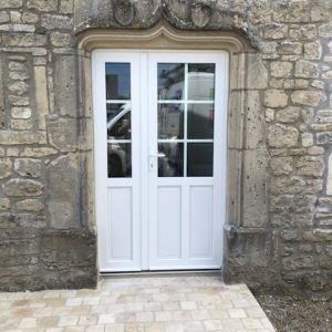Porte double blanche encastrée dans un mur en pierre avec un seuil en pierre carrelée