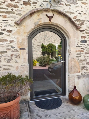 Porte cintrée en pierre avec porte vitrée, plantes en pot et reflet d'une cour