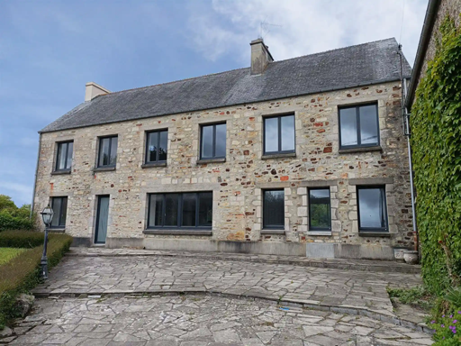 Maison en pierre de deux étages avec de nombreuses fenêtres et une cour pavée sous un ciel nuageux