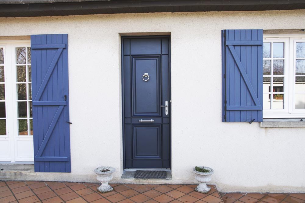 Porte d'entrée bleue avec volets assortis sur une façade de maison blanche