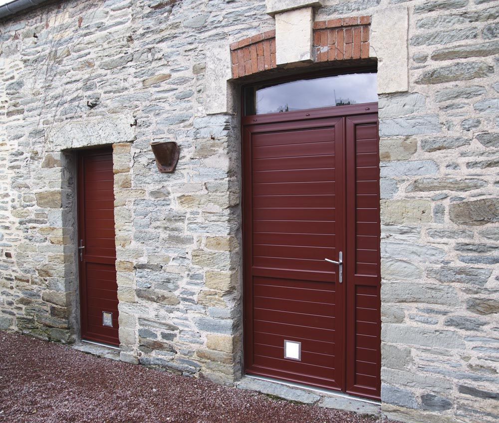 Façade en pierre d'un bâtiment avec deux portes marron, l'une étroite et l'autre plus grande sous un petit auvent.