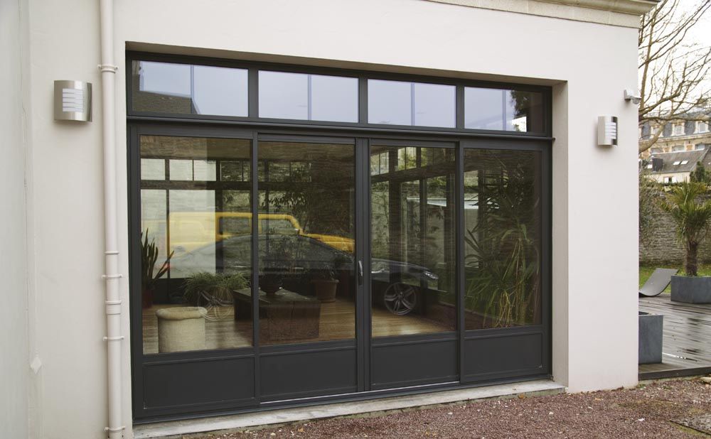 Entrée d'un immeuble moderne avec portes et fenêtres coulissantes en verre foncé sous une façade blanche