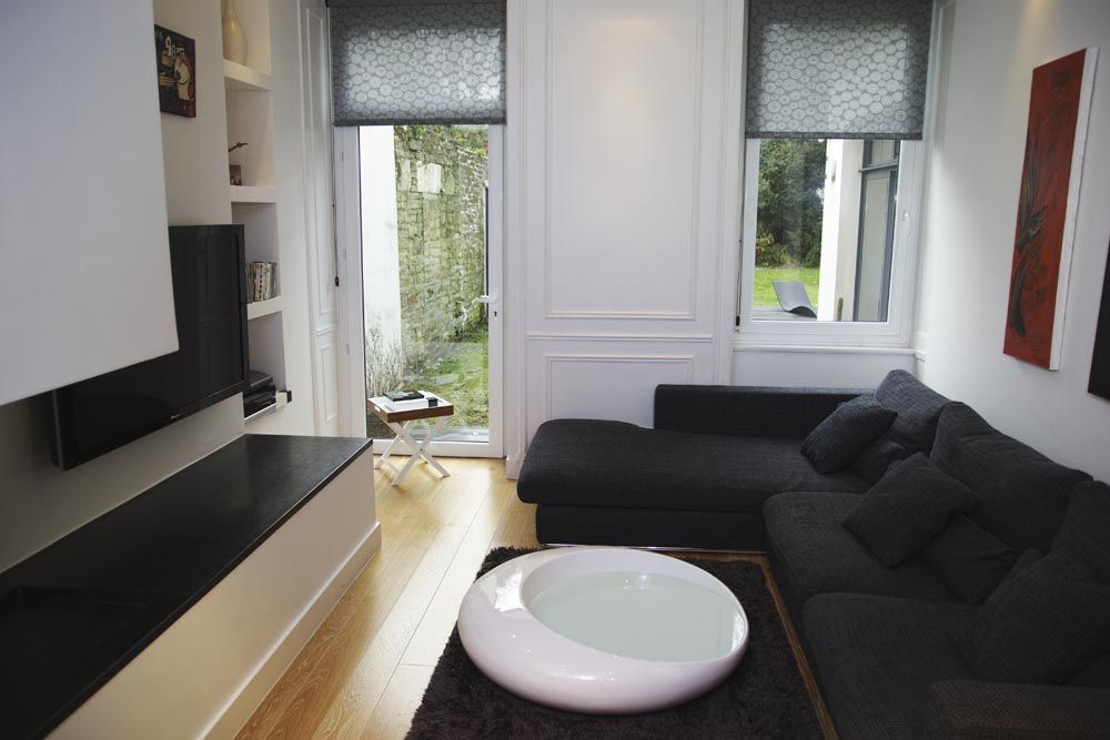 Salon moderne avec canapé foncé, table basse blanche, télévision et porte-fenêtre ouverte donnant sur un jardin.