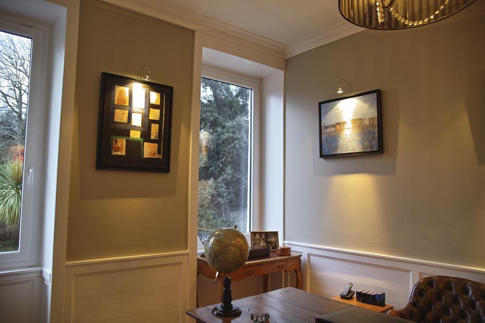 Chambre beige confortable avec des tableaux encadrés, de hautes fenêtres, un globe terrestre sur une table et un fauteuil capitonné.