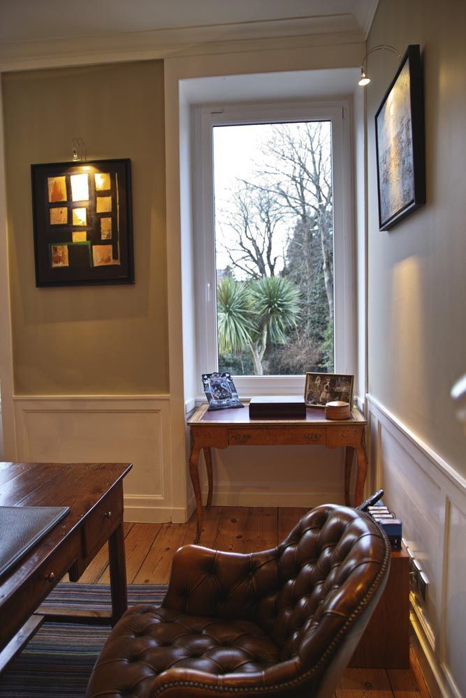 Une chambre confortable avec un fauteuil en cuir capitonné, une table en bois et une vue sur les arbres par la fenêtre.