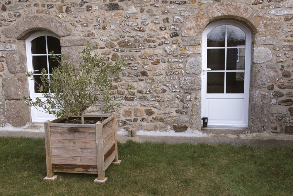 Mur en pierre d'une maison avec deux portes blanches et jardinière en bois sur la pelouse