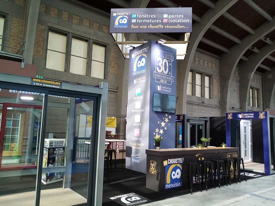 Stand événementiel bleu installé dans le hall d'un immeuble, avec panneaux, comptoir et présentoirs.