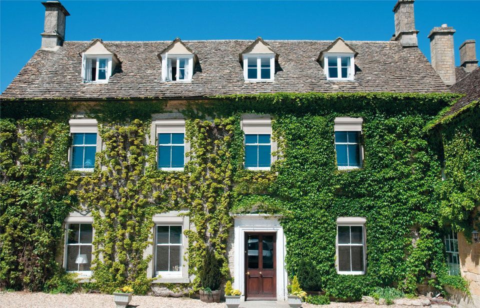 Maison en pierre recouverte de lierre, avec des fenêtres et des lucarnes bleues, sous un ciel d'un bleu éclatant.