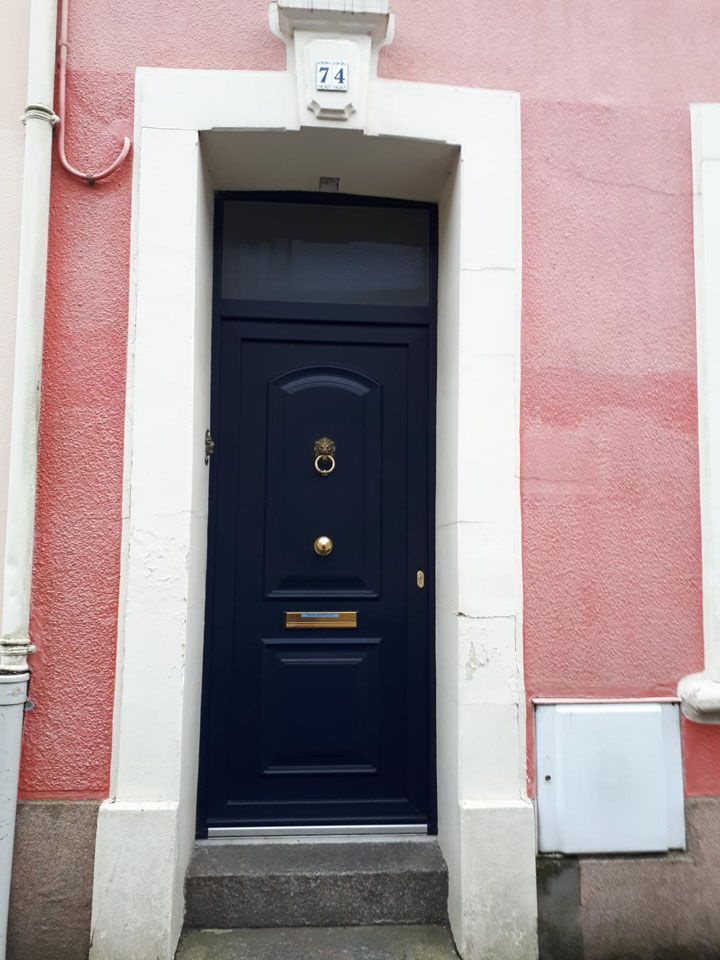 Porte d'entrée bleu marine avec détails en laiton sur une façade en stuc rose, accessible par deux marches en pierre.