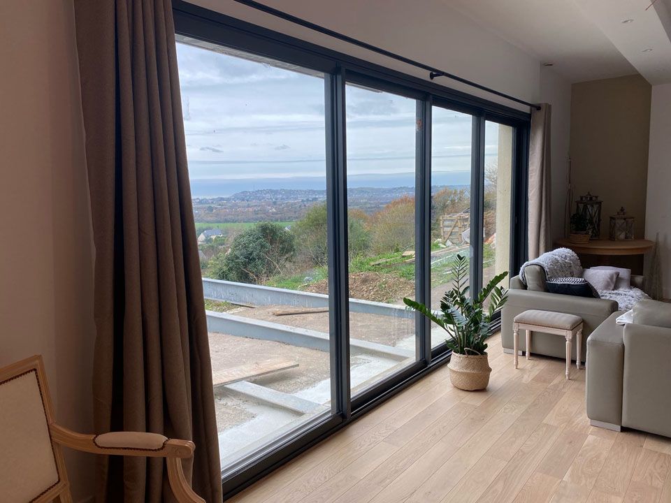 Salon moderne avec baies vitrées offrant une vue imprenable sur une colline et l'eau.