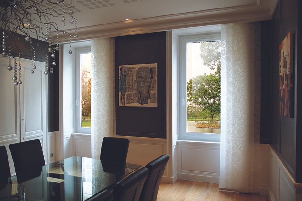 Salle à manger moderne avec table en verre, chaises noires et grandes fenêtres donnant sur les arbres