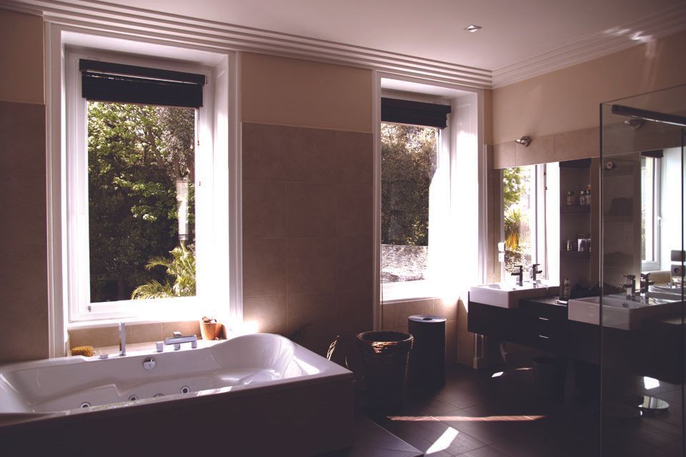 Salle de bains moderne avec baignoire blanche, deux fenêtres et éclairage sombre au-dessus du meuble-lavabo.