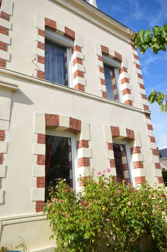 Bâtiment blanc aux façades en briques rouges et aux hautes fenêtres, vu d'un jardin sous un ciel bleu.