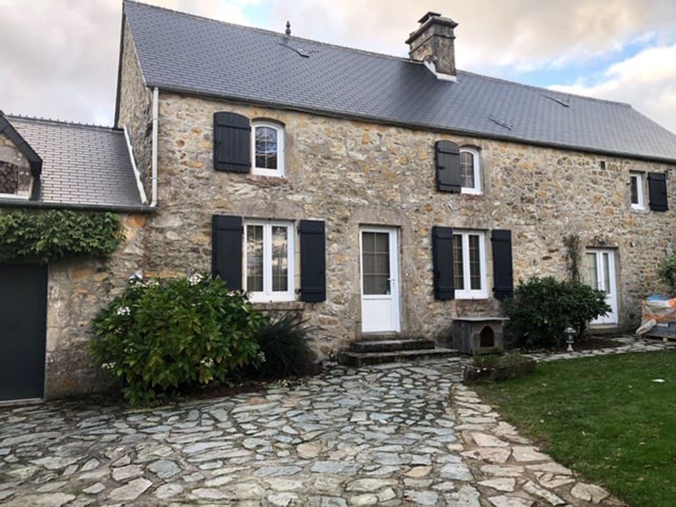 Extérieur de maison en pierre avec fenêtres blanches, marches d'entrée et allée pavée.