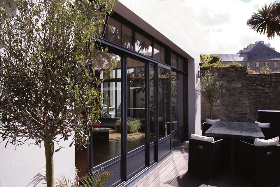 Terrasse avec portes coulissantes en verre, arbre en pot et sièges extérieurs le long d'un mur en pierre