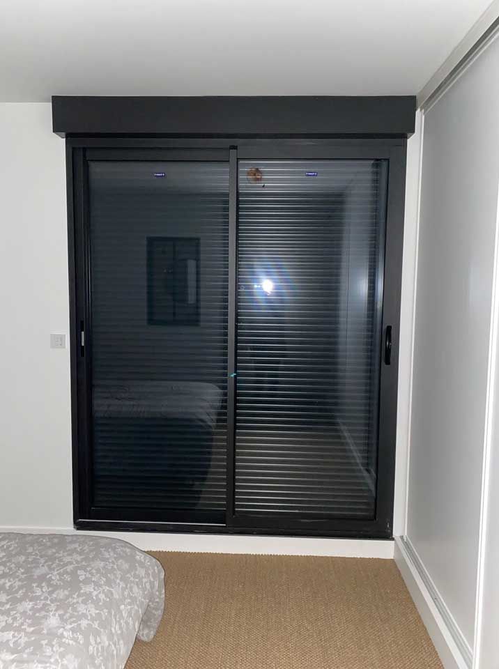 Chambre avec portes coulissantes en verre noir et stores fermés, moquette au sol et murs blancs.