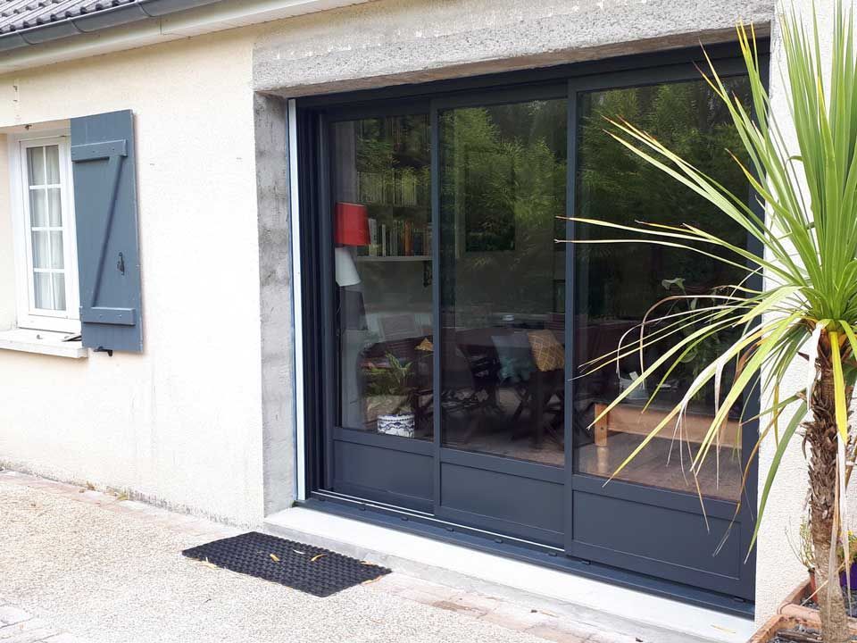 Porte-fenêtre coulissante en verre avec cadre foncé et volets bleus sur l'extérieur d'une maison
