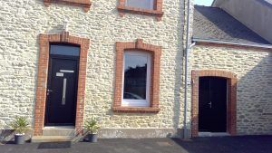 Façade en pierre d'une maison avec portes noires et blanches et fenêtres à encadrement rouge, vue de face