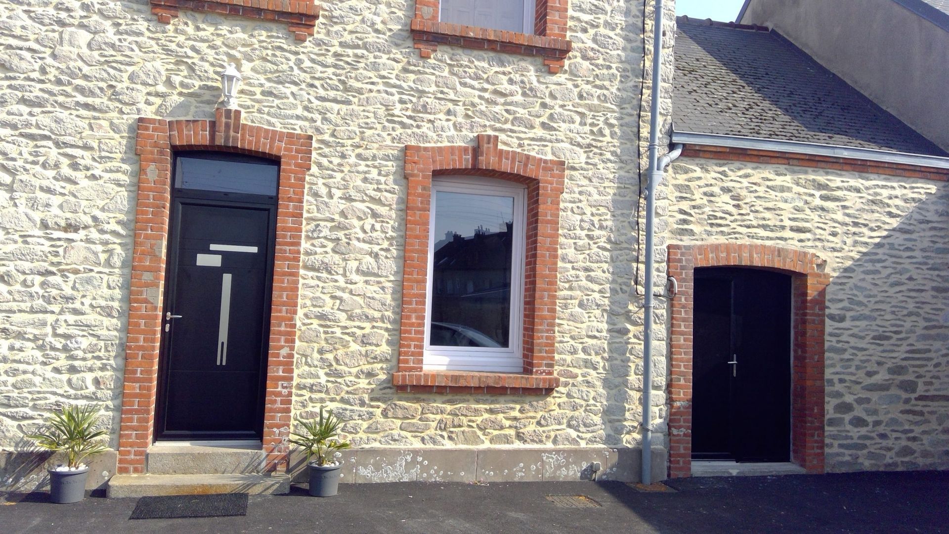 Façade de maison en pierre avec deux fenêtres et deux portes sombres, l'une à gauche et l'autre dans une arche à droite.