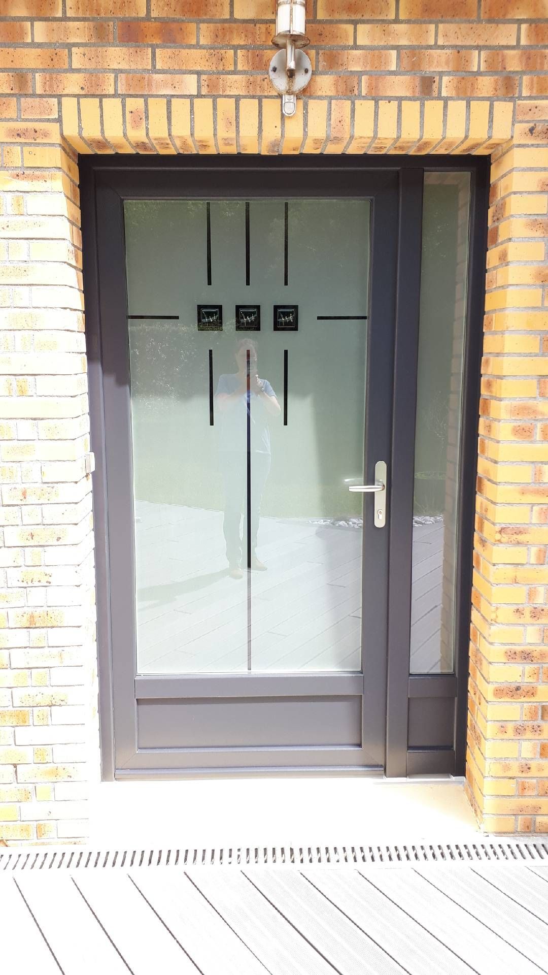 Entrée principale avec une porte vitrée dans un encadrement en briques, surmontée d'un luminaire.