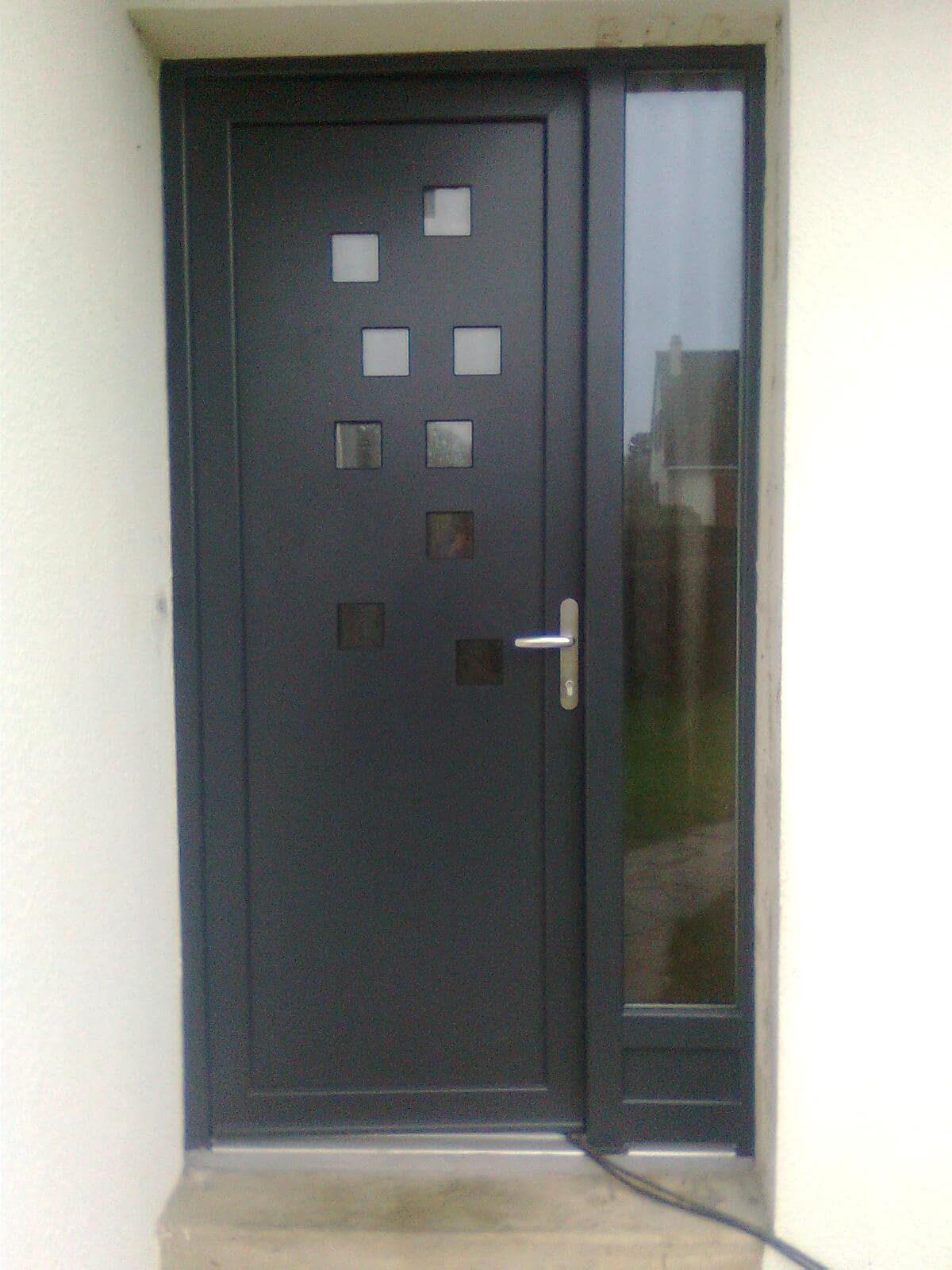 Porte d'entrée noire avec fenêtres carrées de part et d'autre d'un étroit panneau latéral vitré.