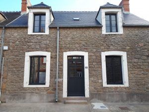 Façade de maison en pierre avec deux lucarnes, porte d'entrée sombre et fenêtres à encadrement blanc