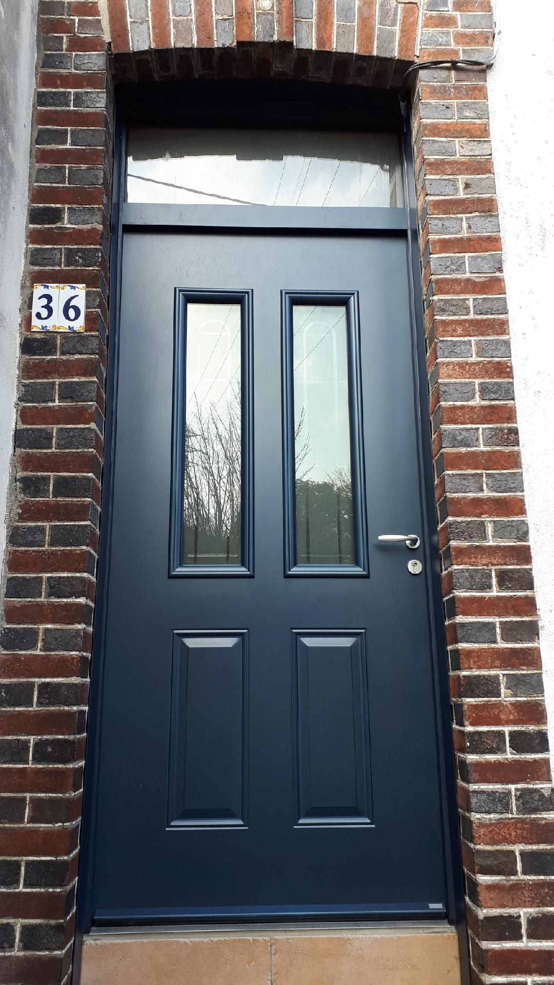 Porte d'entrée bleu foncé avec fenêtres étroites et dépolies dans un encadrement en briques, numéro 36 à gauche