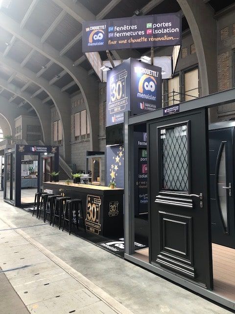 Stand d'exposition modulaire noir avec portes sombres et bannières à l'intérieur d'un grand hall voûté