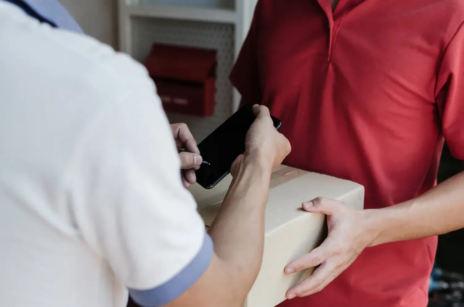 Persona con camisa roja recibe un paquete y firma en un teléfono sostenido por otra persona.