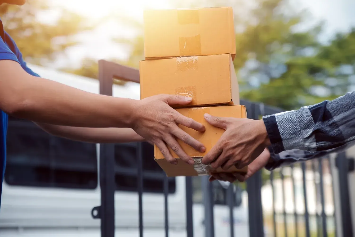 Persona entrega tres cajas de cartón apiladas a otra persona cerca de una puerta.