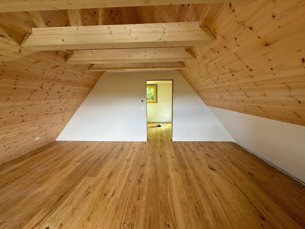 Ein leerer Dachboden mit Holzböden und einer Tür, die zu einem Zimmer führt. Foto von free-tree Roland Gahler Holzmontagen und Schreinerarbeiten