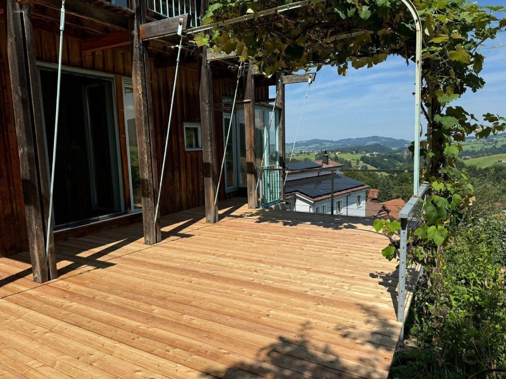 Eine Holzterrasse mit Blick auf ein Haus und die Berge. Foto von free-tree Roland Gahler Holzmontagen und Schreinerarbeiten