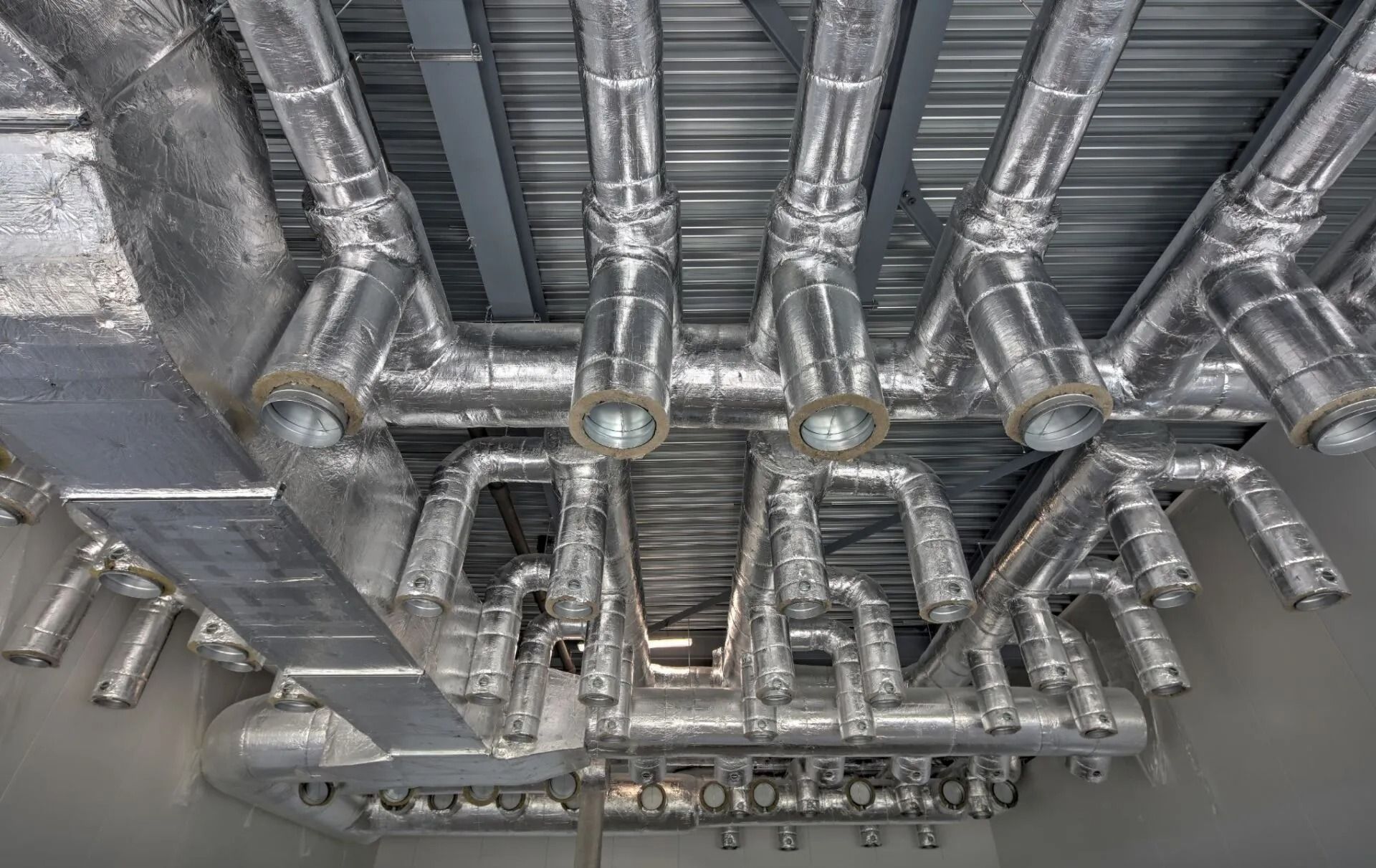 Conduits de CVC isolés en argent le long d'un plafond, avec plusieurs tuyaux et connexions.