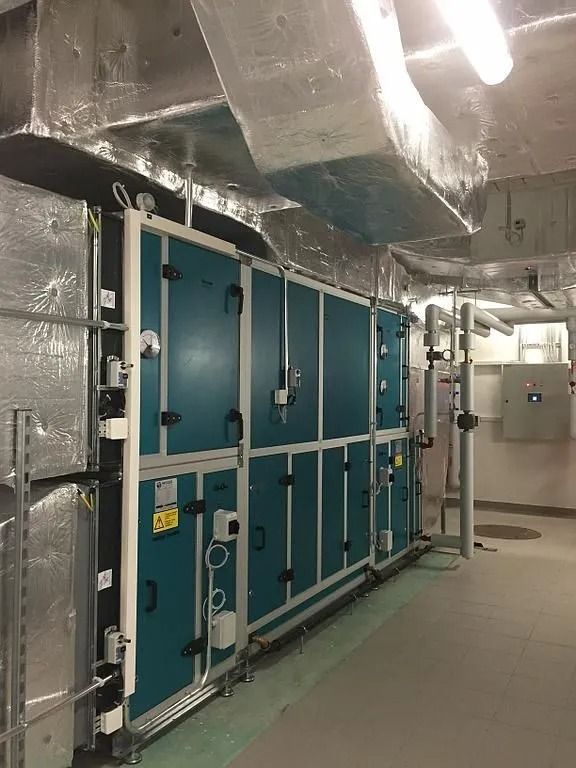 Unité de traitement d'air dans une salle mécanique, avec panneaux bleu sarcelle et conduits argentés.