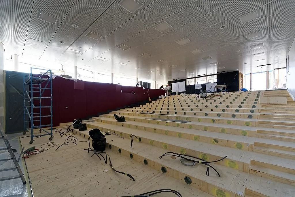 Auditorium en construction ; gradins en bois, mur rouge, plafond argenté, échelles, outils.