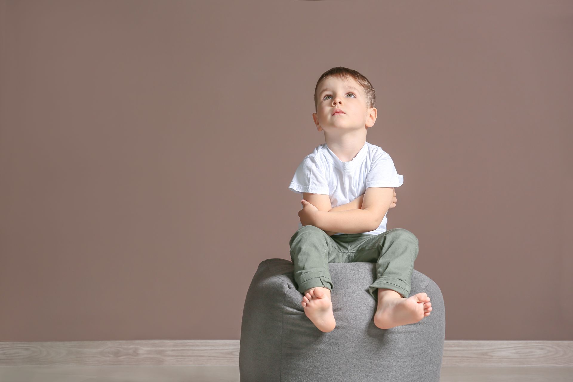 Garçonnet assis sur un pouf avec les bras croisés et les yeux vers le ciel - Sonia Bahouth psychologue, Cabinet Sagita
