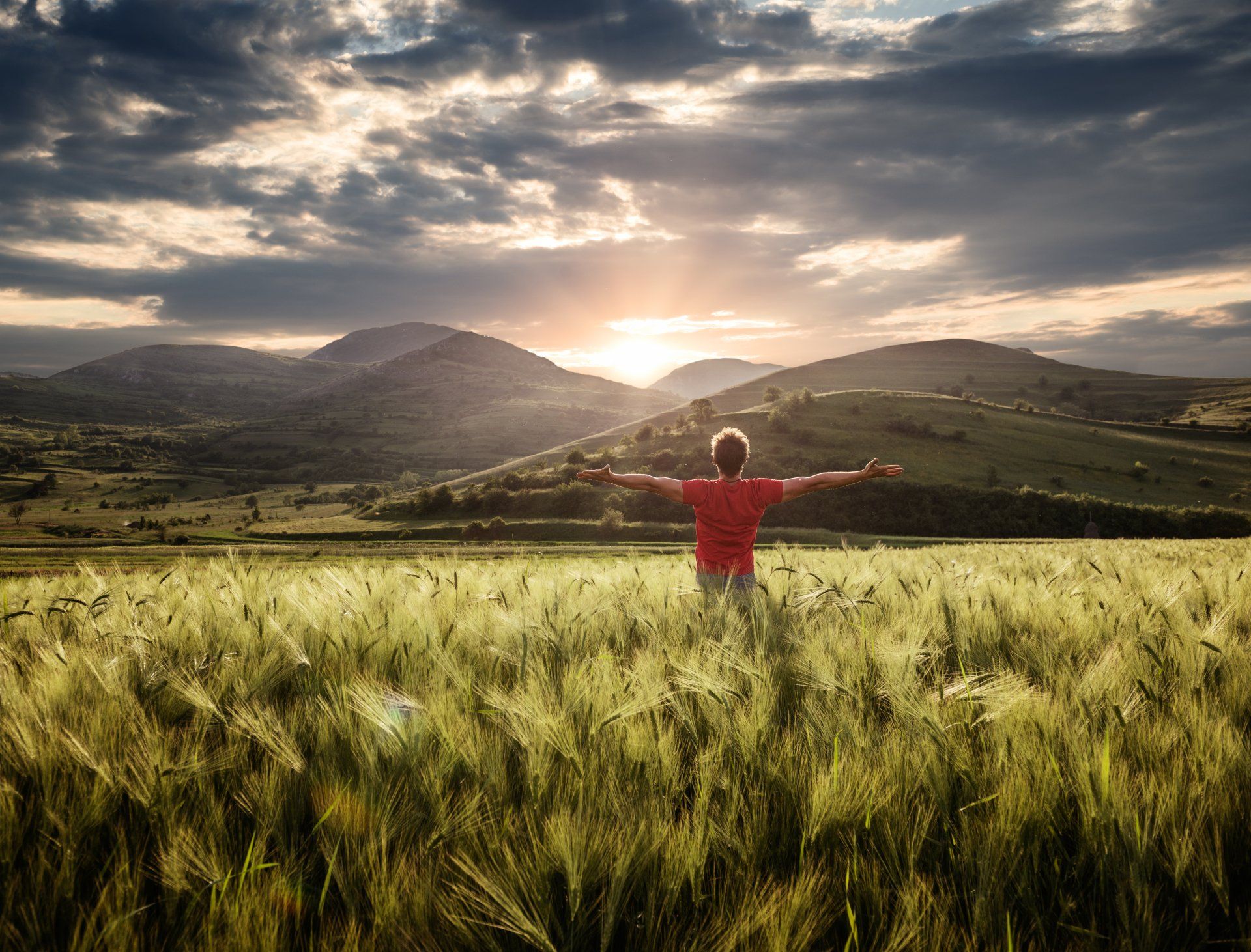 Homme dans un champ de blé, bras grands ouverts, devant un coucher de soleil - Sonia Bahouth psychologue, Cabinet Sagita